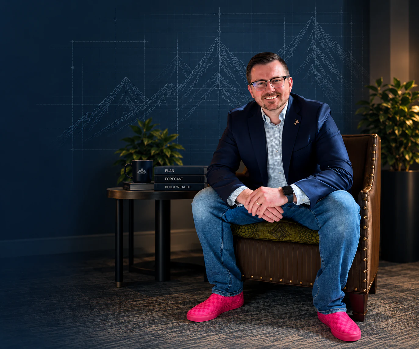Ashley Skinner, founder of Capehelm, seated beside a table against a navy blueprint mountain backdrop